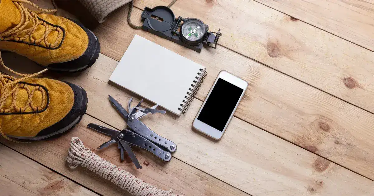 Survival gear and camping equipment organised on a flat surface including backpack, tools, and supplies for a 72-hour bag